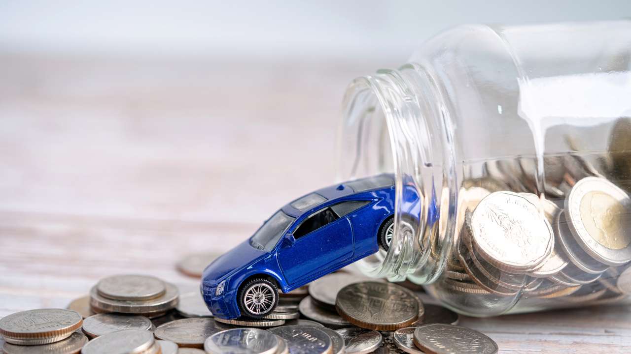 mini auto diagonaal uit een glazen pot met kleingeld