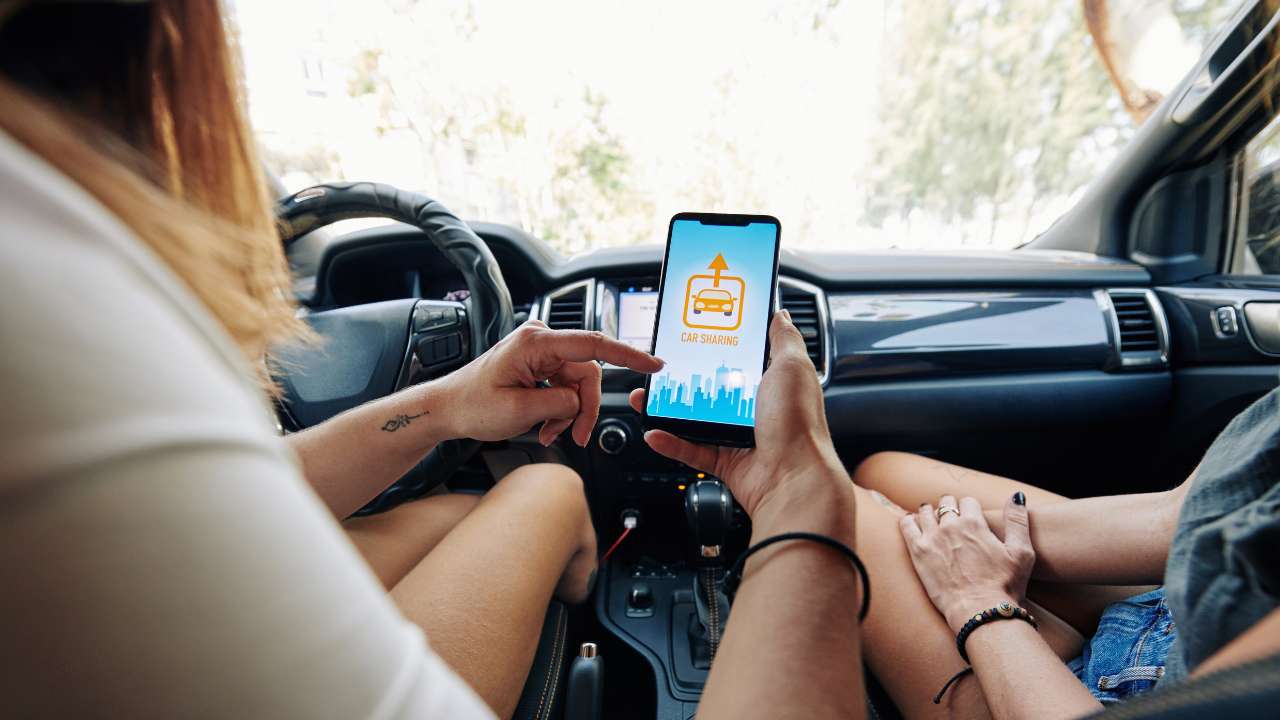 2 personen in een auto met telefoon waar car sharing op het scherm staat