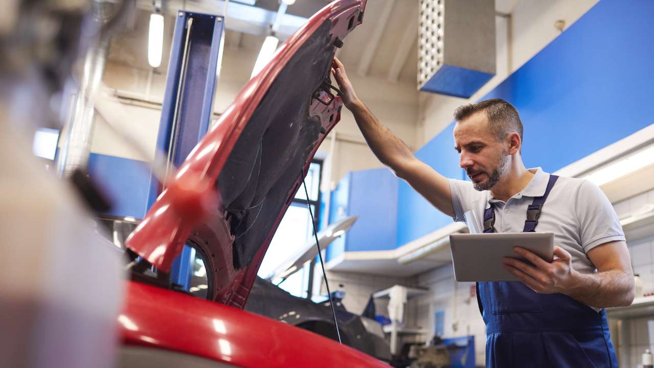 man kijkt onder motorkap auto met notitieblok in zijn hand
