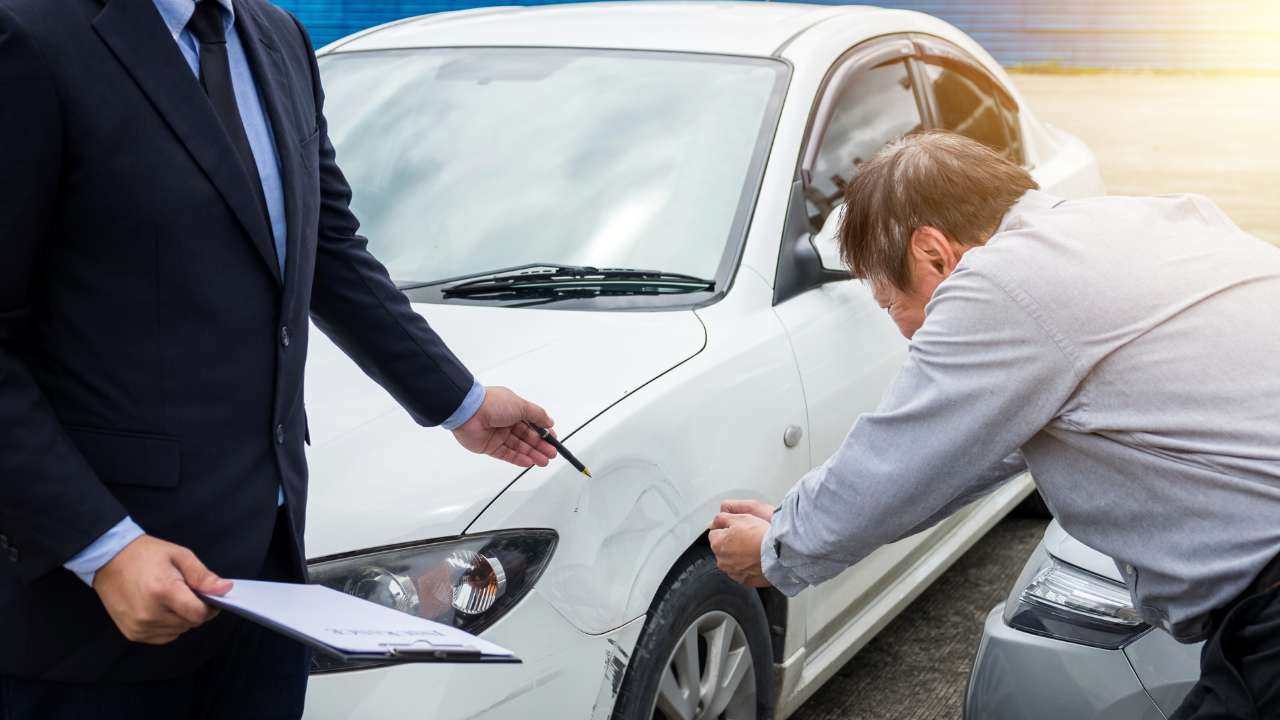 man wijst naar schade op zijn auto en iemand die een clipboard vastheeft