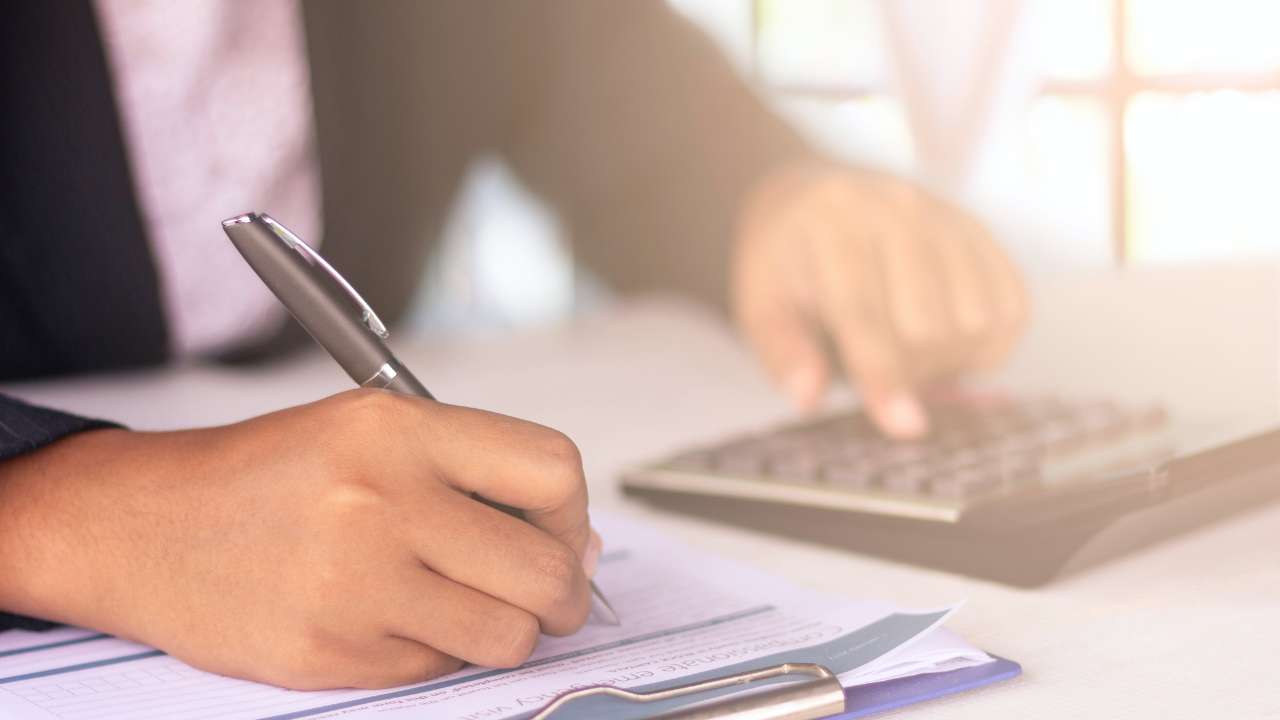 paar handen van iemand in pak, een met een pen aan het schrijven andere bezig op een calculator
